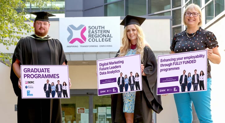 Graduation Programmes, three people holding boards outside campus building 